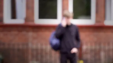 A blurred picture of a teenage boy in a school uniform. Specific details are difficult to make out.