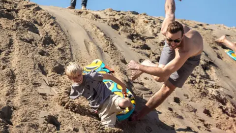 Getty Images Uncle and nephew sled down a sand dune in Hermosa Beach, California, on 26 November 2020