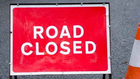 A red "road closed" sign on a road. 
