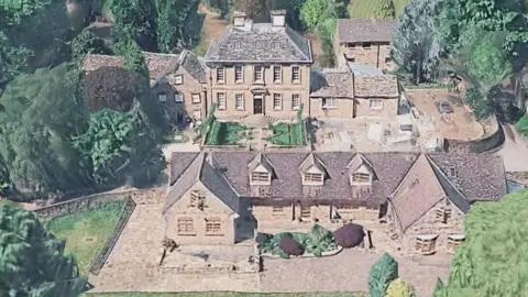 This is an image of an historic home.  The picture is taken from the air and shows a substantial home built out of sandstone with a  grey slate roof.  There are also smaller properties around the dwelling.