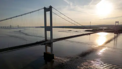 A drone image taken from the side of the Severn Bridge, and a sunset overlooking it.