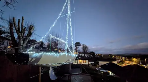 A large yacht, covered in white fairy lights. It sits against a dark sky 