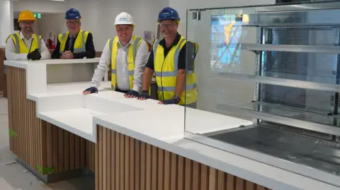 Four men in hard hats behind a new counter. The men are smiling at the camera. 