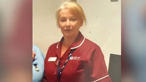 Johnston family Monica Johnston in her red nurses uniform, she has short blonde hair.