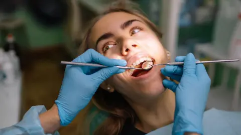 Getty Images female patient lying in dental chair with mouth open during treatment