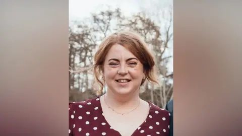 Suffolk Police A head and shoulders image of a woman wearing a burgundy and white polka dot top. She is smiling and looking into the camera.