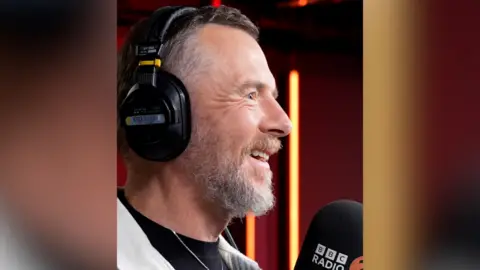 A man wearing headphones speaks into a microphone.