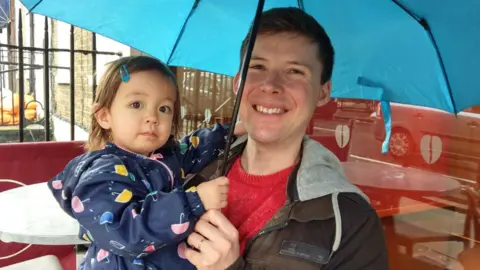 Matthew and his daughter under an umbrella