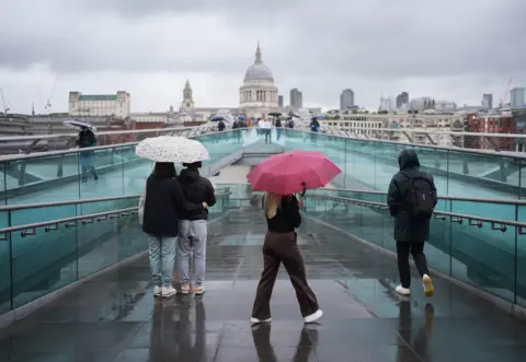 People with umbrellas walking along a bridge on a rainy day in London. 
