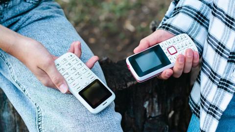 Small push-button mobile phones pictured in the hands of teenagers outdoors