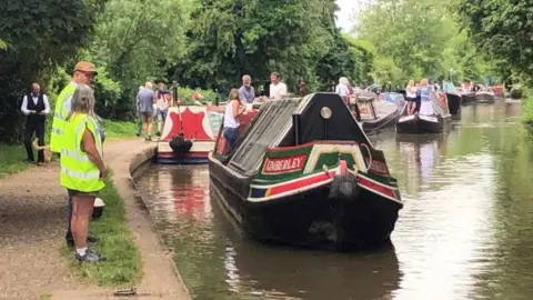 BBC/Martin Heath Collection of narrowboats with people aboard the boats and on the towpath