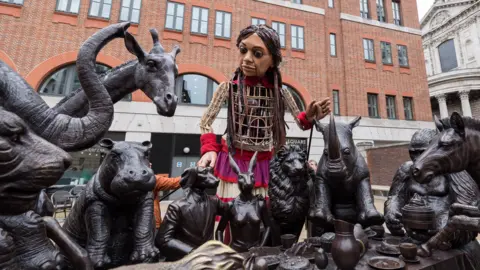 Getty/Anadolu Little Amal stood with a statue of various animals