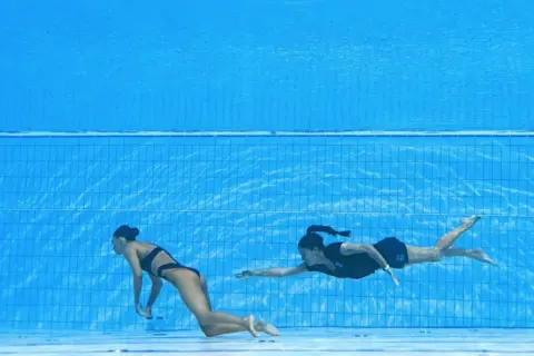 OLI SCARFF / AFP SA's coach Andrea Fuentes (R) swims to recover USA's Anita Alvarez (L), from the bottom of the pool during an incident in the women's solo free artistic swimming finals, during the Budapest.