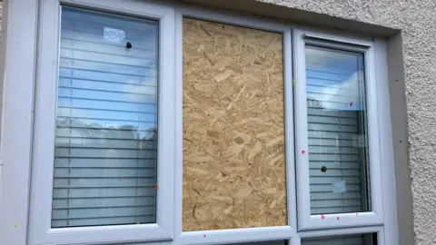 A middle window pane is boarded between two glass windows 