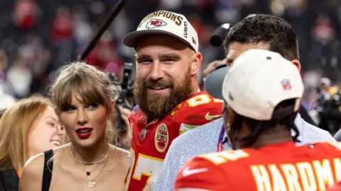 Getty Images Travis Kelce (centre) with his girlfriend Taylor Swift after the Kansas City Chiefs won the Super Bowl earlier this year