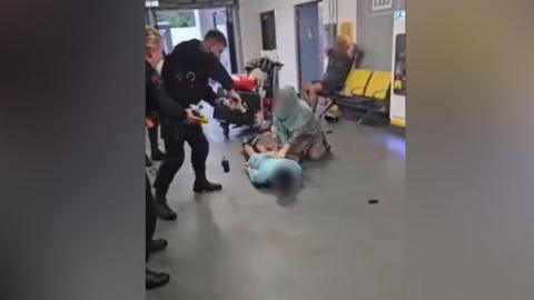 Police officer standing over a man whose face is blurred out lying on the ground