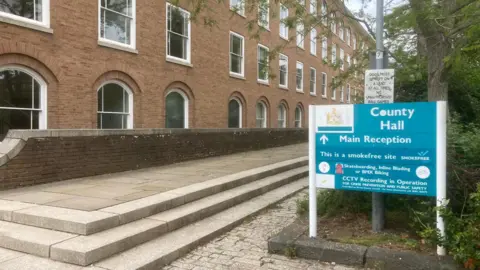 Devon County Hall is seen with a signpost in the foreground.