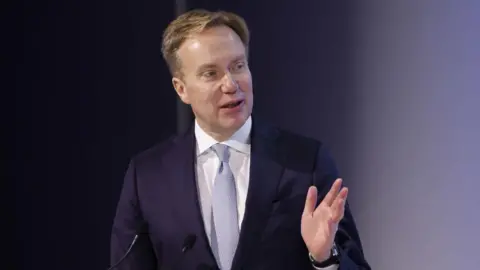 Getty Images Borge Brende, president of the World Economic Forum, speaks in front of two small microphones, wearing a navy blue suit