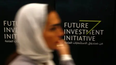 Reuters A woman walks past a sign during the Future Investment Initiative conference in Riyadh, Saudi Arabia (24 October 2017)