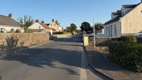 Route Millitaire - A long tarmac road with houses on either side. 
