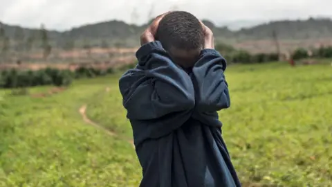 AFP via Getty Images A man in a black sweat shirt holds his head in grief after losing his relatives in an attack by Fulani herders near Jos. Behind him is greenery and hills in the distance. Archive shot.