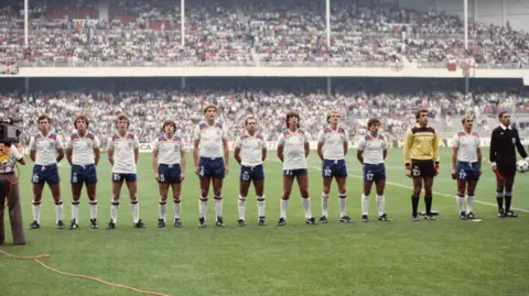 Getty Images The England team, kitted out in their Admiral strips, look on during the national anthems before their 1982 FIFA World Cup Second Round Group match against Spain at Santiago Bernabeu Stadium. 
