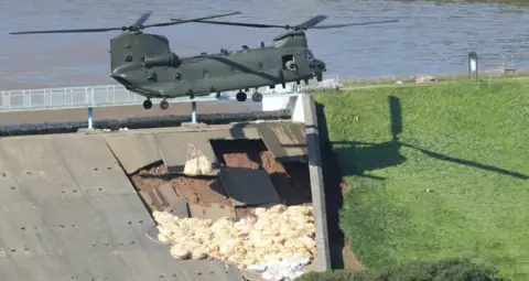 Danny Lawson/PA Media A chinook helicopter dropping beige bags on the side of a dam