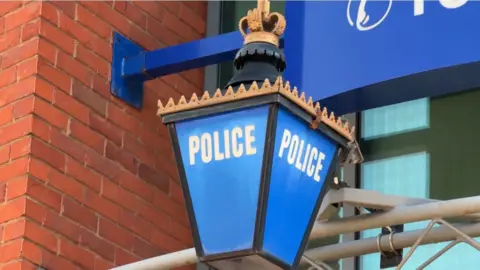 A blue four sided police light hangs from a police building. There is a crown attached to the top of the light.