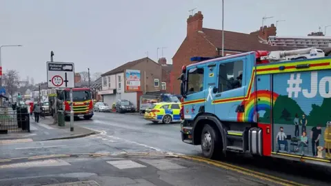 Samantha Doughty A busy road in central Hull with shops and residential houses on each side. A blue fire truck can be seen on the right, along with a red one further up the road. A police car is also parked in the middle of the road.