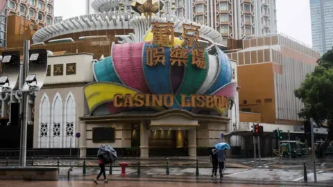 AFP Pedestrians walk past Casino Lisboa in Macau which has closed because of Typhoon Mangkhut on 16 September 2018