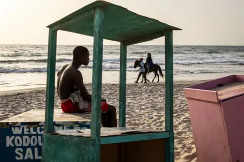 JOHN WESSELS/AFP A young man looks as a woman takes a horse ride along a beach in Banjul.