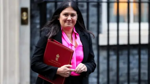 Reuters Nandy, in a pink shirt and black suit, walks outside No 10 carrying a red folder branded with the Department of Media and Culture in gold.