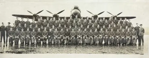 Gildings Auctioneers Black and white photograph of RAF personnel posed in front of a Lancaster bomber, with its cockpit, wings and four engines in view.