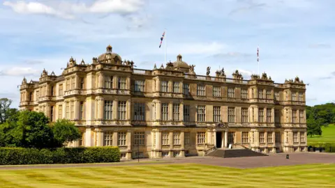 Getty/Andrew_Harker A view of Longleat House on a sunny day. Huge light-stoned stately home with dozens of big windows and octagonal domes on top. Large green lawn in front.