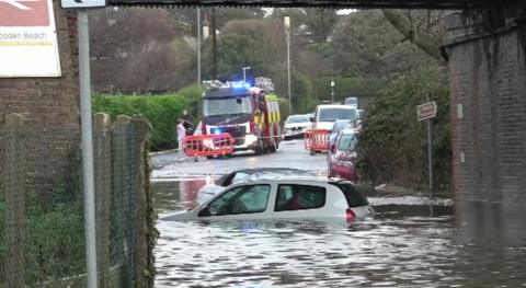 A car with flood-water up to its windows, underneath a railway bridge 