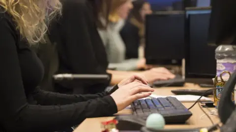 A woman is sitting at a computer and typing on a keyboard.