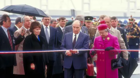 Eurotunnel The French president, Francois Mitterrand, and Queen Elizabeth II cut a red, white and blue ribbon as multiple other dignitaries, including Prince Philip and John Major, wtach on. The queen is wearing a bright pink coat.