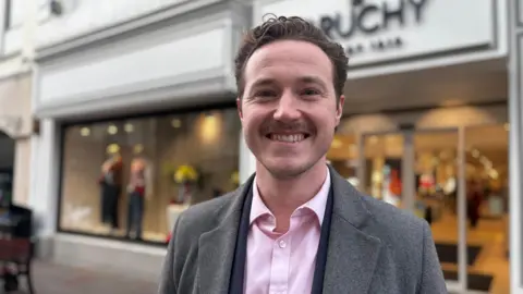 A man standing with a clothing building behind him.