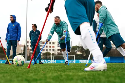 Manon Cruz/Reuters Amputee footballers attend a training session. Six men are pictured. Three are amputees on crutches. The football is to the left of the picture and two of the men on crutches are looking at it.