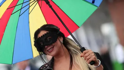 PA A woman with a face mask holding a brightly coloured umbrella
