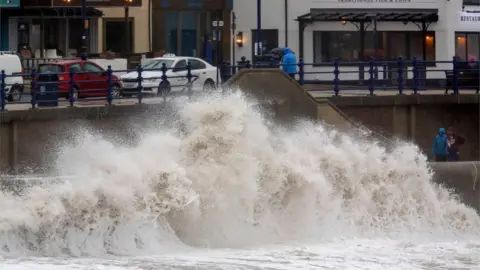 Getty Images Pedestrians walk along the promenade as huge waves crash