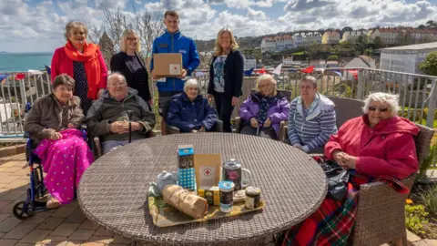 Le Platon Home Elderly people sat round a table with the contents of a hamper on the table