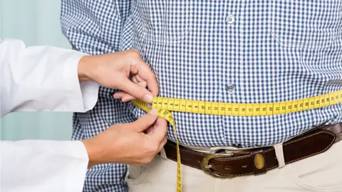 Getty Images Man having his waistline measured