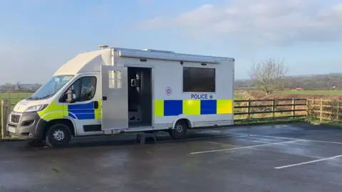 A large police lorry with the side door open on a car park by a field