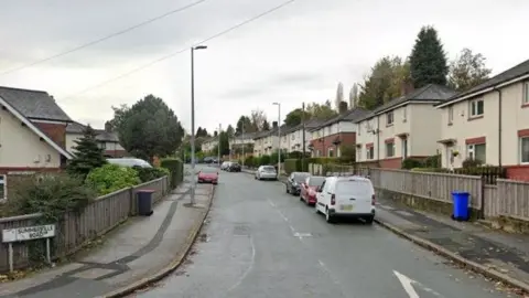 Houses are either side of a road. A sign on the left hand side says Summerville Road. There are seven cars parked along the road, along with a van.