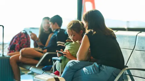 Girl and woman sitting an airport departure gate