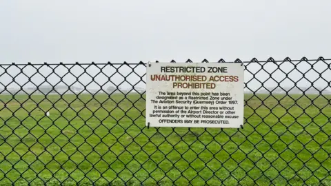A sign which said Restricted Zone Unauthorised Access. On a black wire fence. 