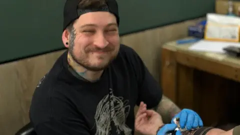 Martin Moore A man smiling while doing a tattoo on someone's arm