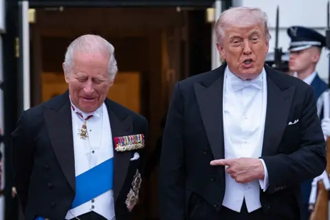 AFP via Getty Images Donald Trump points his finger at a laughing King Charles as they stand side by side before entering a State Dinner at Washington DC. The two are wearing tailcoats and white shirts, while King Charles also has a blue sash.