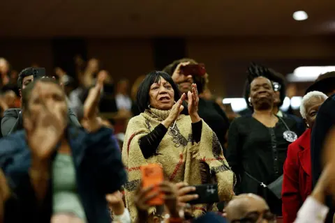 Getty Images Attendees, including one woman centered in the image are standing up and clapping.